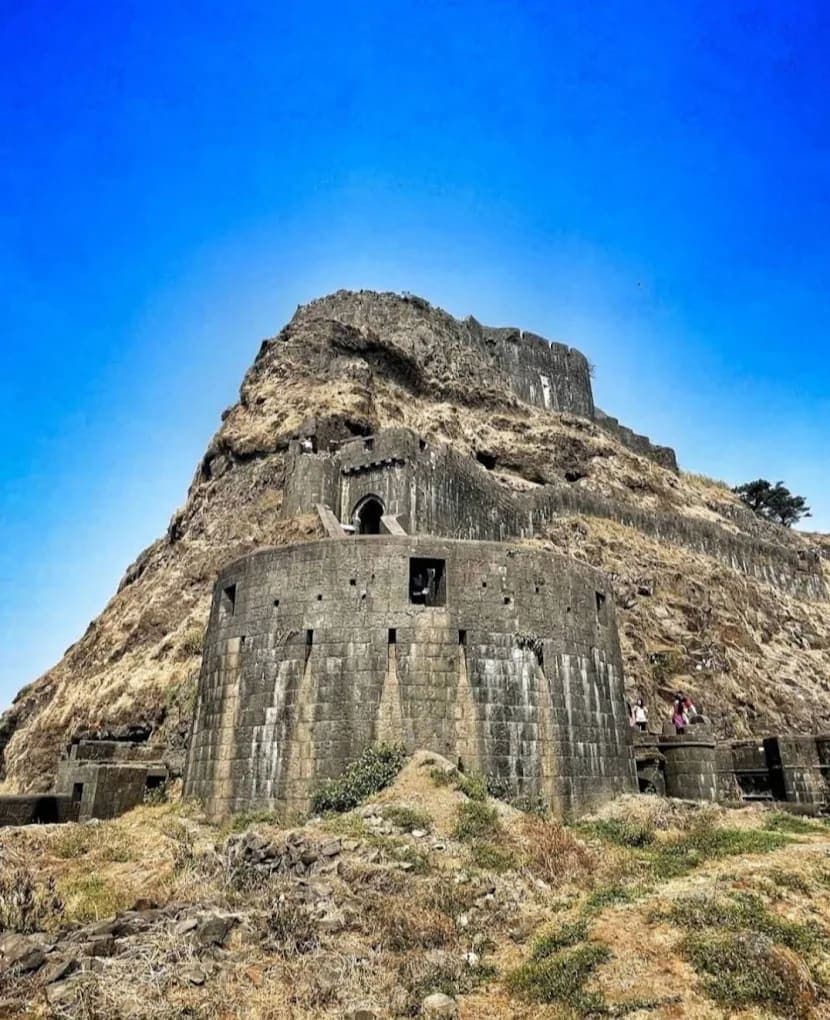 Panoramic view of Sinhagad Fort's massive stone ramparts and the Pune city skyline in the distance
